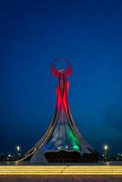 uzbekistán, Tashkent - mayo 5, 2023 iluminado Monumento de independencia en el formar de un estela con un humo pájaro, fuentes y ondulación banderas en el nuevo Uzbekistán parque a Noche. foto