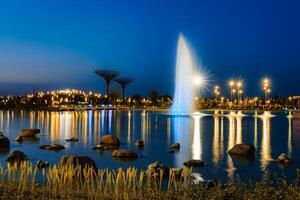 Blurred fountain water flows in an artificial lake in a night park with lanterns and decorations. photo