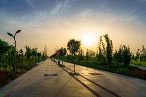 City park in early summer or spring with pavement, lanterns, young green lawn, trees and dramatic cloudy sky on a sunset or sunrise. photo