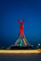 uzbekistán, Tashkent - mayo 5, 2023 iluminado Monumento de independencia en el formar de un estela con un humo pájaro, fuentes y ondulación banderas en el nuevo Uzbekistán parque a Noche. foto