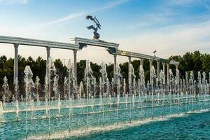 Memorial and rows of fountains illuminated by sunlight at sunset or sunrise in the Independence Square at summertime, Tashkent. photo