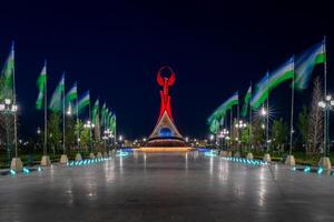 uzbekistán, Tashkent - mayo 5, 2023 iluminado Monumento de independencia en el formar de un estela con un humo pájaro, fuentes y ondulación banderas en el nuevo Uzbekistán parque a Noche. foto