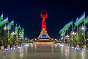 uzbekistán, Tashkent - mayo 5, 2023 iluminado Monumento de independencia en el formar de un estela con un humo pájaro, fuentes y ondulación banderas en el nuevo Uzbekistán parque a Noche. foto