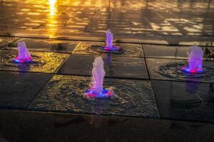 Small fountains on the sidewalk, illuminated by sunlight at sunset or sunrise at summertime. photo