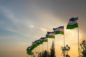banderas de Uzbekistán ondulación en un puesta de sol o amanecer dramático cielo antecedentes. foto