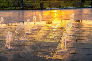 Small fountains on the sidewalk, illuminated by sunlight at sunset or sunrise at summertime. photo