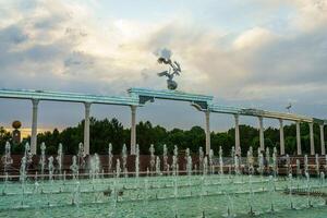 monumento y filas de fuentes iluminado por luz de sol a puesta de sol o amanecer en el independencia cuadrado a Hora de verano, Taskent. foto