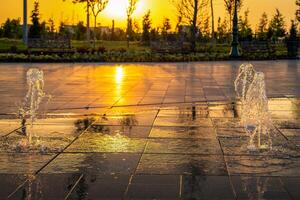 Small fountains on the sidewalk, illuminated by sunlight at sunset or sunrise at summertime. photo