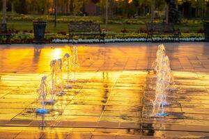 Small fountains on the sidewalk, illuminated by sunlight at sunset or sunrise at summertime. photo