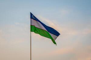 bandera de Uzbekistán ondulación en un puesta de sol o amanecer dramático cielo antecedentes. foto