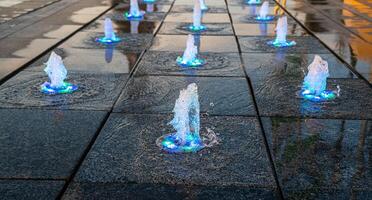 Small fountains on the sidewalk, illuminated by sunlight at sunset or sunrise at summertime. photo