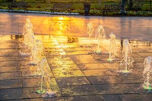 Small fountains on the sidewalk, illuminated by sunlight at sunset or sunrise at summertime. photo