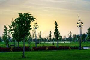 City park in early summer or spring with lanterns, young green lawn, trees and dramatic cloudy sky on a sunset or sunrise. photo