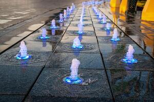 Small fountains on the sidewalk, illuminated by sunlight at sunset or sunrise at summertime. photo