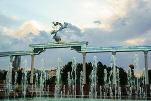 monumento y filas de fuentes iluminado por luz de sol a puesta de sol o amanecer en el independencia cuadrado a Hora de verano, Taskent. foto