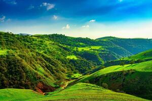 Hills and mountains covered with young green grass and illuminated by the sun on a sunny day. photo