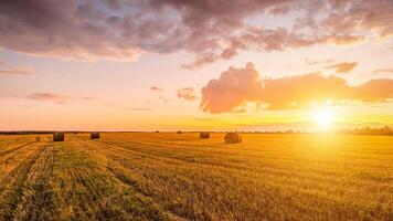 Scene of sunset on the field with haystacks in Autumn season. Rural landscape with cloudy sky background. photo