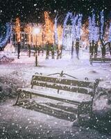 Snowfall in a winter park at night with decorations, glowing lanterns, pavement covered with snow and trees. Vintage film aesthetic. photo