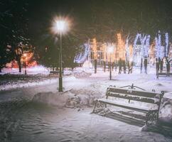 invierno parque a noche con Navidad decoraciones, brillante linternas, pavimento cubierto con nieve y arboles Clásico película estético. foto