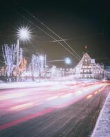 noche invierno ciudad con Navidad o nuevo año decoraciones, abeto y huellas de faros de Moviente carros. Clásico película estético. foto