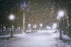 nevada en un invierno parque a noche con brillante linternas, pavimento cubierto con nieve y arboles Clásico película estético. foto