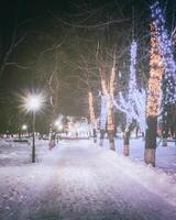 invierno parque a noche con Navidad decoraciones, brillante linternas, pavimento cubierto con nieve y arboles Clásico película estético. foto