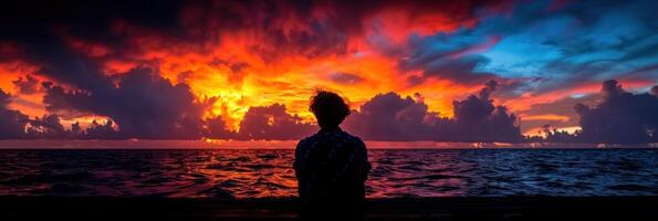 A man stands facing a vibrant sunset in a picturesque landscape photo