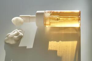 Beige facial foam with a dispenser and brush in the rays of the setting sun. photo