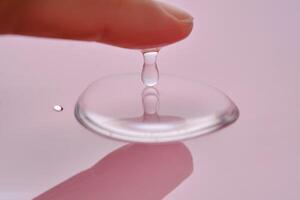 A finger touches a drop of cosmetic product on a pink background. photo