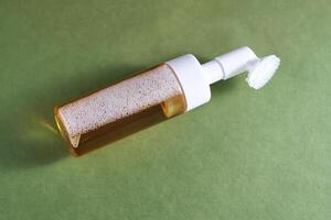 Beige facial foam with a dispenser and brush in a green background. photo