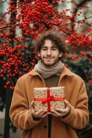 Smiling young man in a winter coat holding a Christmas gift with a red ribbon outdoors photo