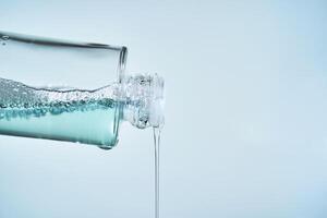 Cosmetic bottle from which serum is pouring on a blue background. photo