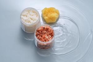 Body scrub, bath salt and natural sponge on a blue background with water. photo