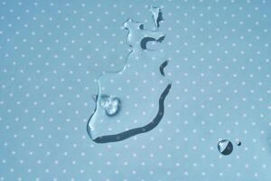 A drop of water or cosmetic serum on a blue polka dot background. photo