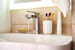 Bathroom sink with toothbrushes and running water. photo