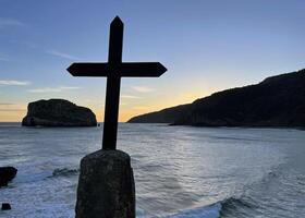 Oceanfront at San Juan de Gaztelugatxe in Spain during sunrise with a cross in the foreground photo