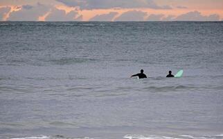 Two surfers waiting for the perfect wave during sunset in Spain photo