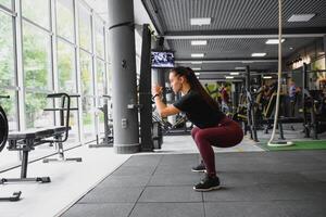 lado ver retrato de un joven mujer haciendo sentadillas a aptitud gimnasia. foto