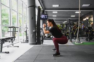 Side view portrait of a young woman doing squats at fitness gym. photo