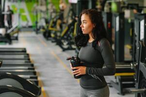 Young beautiful woman drinking water in sports gym. photo
