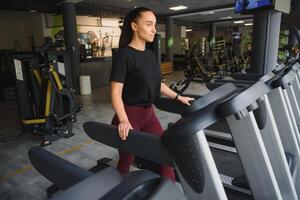atractivo joven Deportes mujer es trabajando fuera en gimnasia. haciendo cardio formación en rueda de andar. corriendo en rueda de andar foto