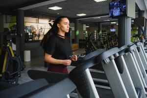 Woman trains on a treadmill in the gym. Young fitness girl running on treadmill machine. Sports exercises for weight loss photo