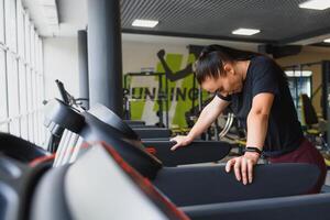 Portrait of a woman resting after her workout. She is leaning on a treadmill and looks completely exhuasted photo