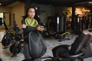 Young woman drinking water and taking a break after workout in gym photo