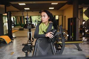 joven mujer Bebiendo agua y tomando un descanso después rutina de ejercicio en gimnasio foto