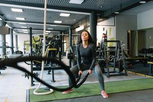 bonito Hispano joven mujer haciendo algunos crossfit ejercicios con un cuerda a un gimnasia. foto