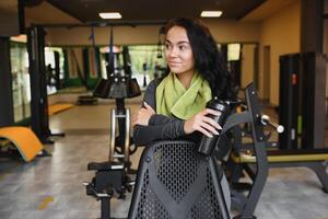 joven mujer Bebiendo agua y tomando un descanso después rutina de ejercicio en gimnasia, foto