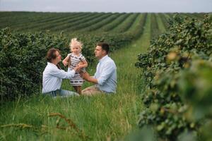 The daughter hugging parents on nature. Mom, dad and girl toddler, walk in the grass. Happy young family spending time together, outside, on vacation, outdoors. The concept of family holiday photo