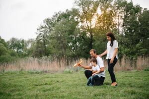 padre, madre y hijo jugando con juguete avión en el parque. simpático familia. personas teniendo divertido al aire libre. imagen hecho en el antecedentes de el parque y azul cielo. concepto de un contento familia foto