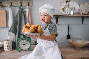 Young boy cute on the kitchen cook chef in white uniform and hat near table. homemade gingerbread. the boy cooked the chocolate cookies. photo